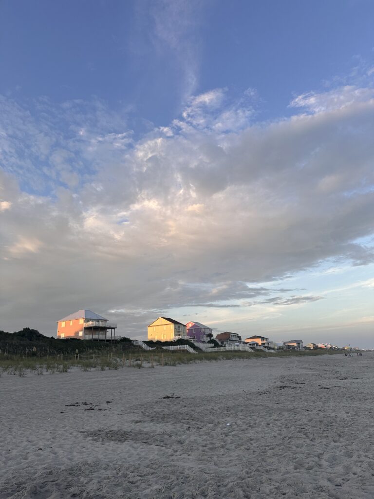 Brightly colored houses line a beach with the sunsetting above them